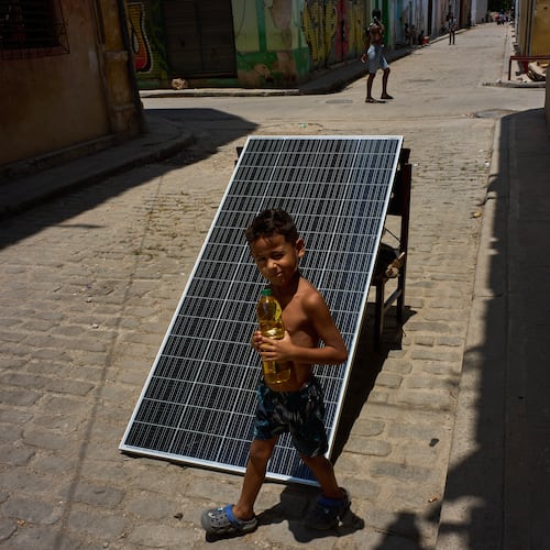 A child walks with a bottle of oil past a solar panel set up on the street to charge batteries during a blackout in Havana, Cuba, Monday, July 6, 2026. (AP Photo/Ramon Espinosa)