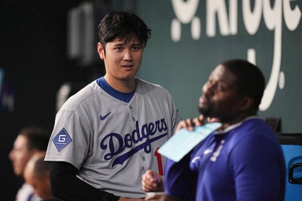 Los Angeles Dodgers' Shohei Ohtani talks with a staff member in the dugout in the seventh inning of a baseball game against the Texas Rangers in Arlington, Texas, Sunday, April 20, 2025. (AP Photo/Tony Gutierrez)