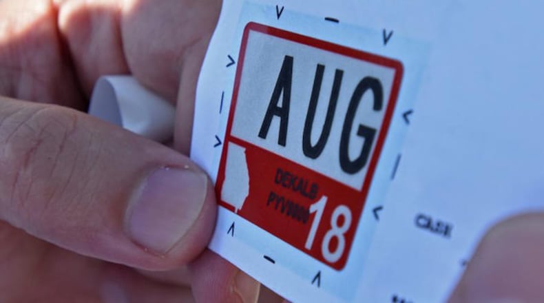 Mohamed Al Ali holds a registration sticker before he attaches it to his license plate in the parking lot of the Motor Vehicle Division of the DeKalb County Tax Commissioner North Office on Wednesday, July 26, 2017.