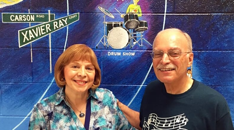 John LaMattina and his wife, Roseann, frame a Norton Elementary School mural that features his drum program. LaMattina recently held his final concert for the program, which he has taught for free at the school since 1988.