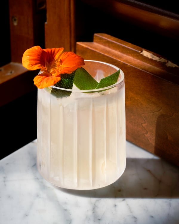 A milky-looking cocktail in a round rocks glass, garnished with a tropical flower and a twist of lime peel.