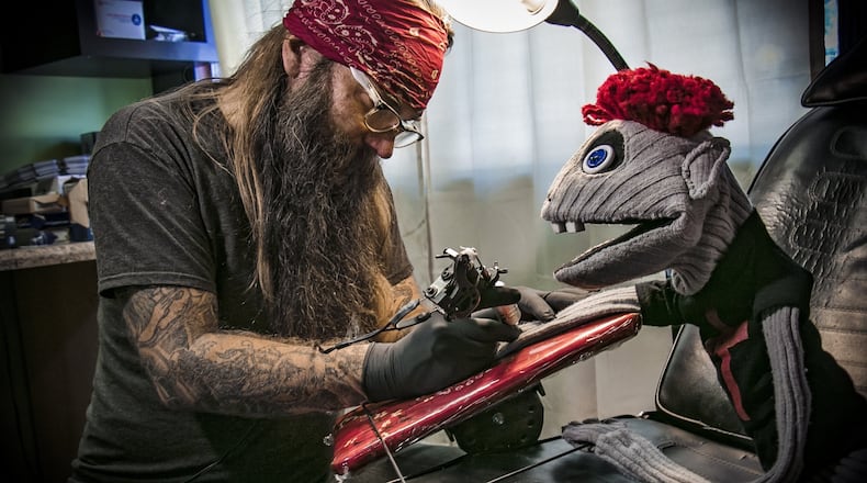 Tyrone, a bad puppet from the Alliance Theatre production “Hand to God,” decides it’s time to get a tattoo on his cloth arm from artist Jett Bryant. CONTRIBUTED