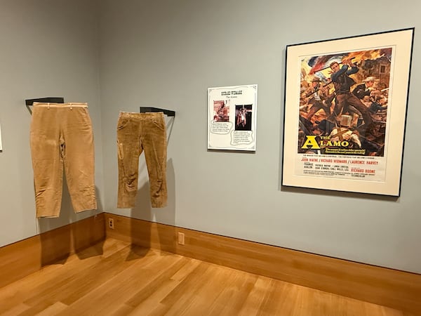 Pants worn by John Wayne and Richard Widmark in "The Alamo" are on display next to a poster for the 1960 film. (Danielle Charbonneau/AJC)
