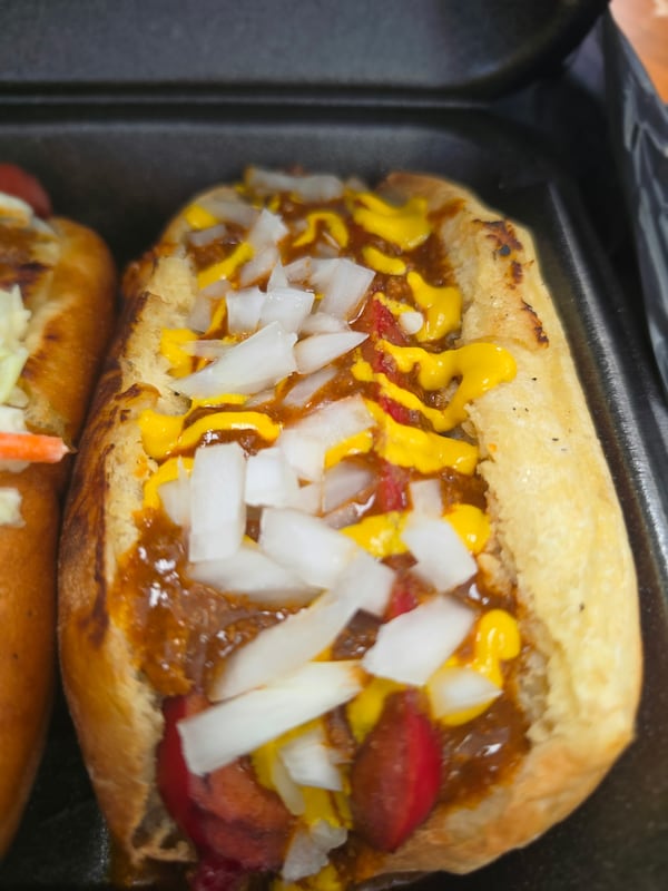 Two hot dogs loaded with toppings, including dhopped onions, chili, yellow mustard and ketchup.