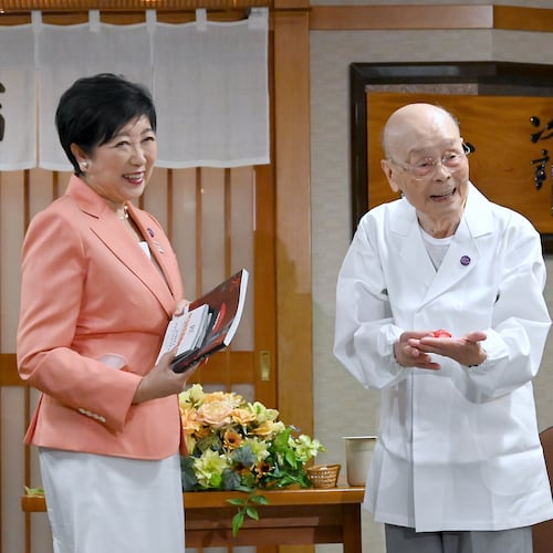 In this photo released by Bureau of Social Welfare, Tokyo Metropolitan Government, sushi legend Jiro Ono, right, shows a gift from Tokyo Gov. Yuriko Koike to celebrate his 100th birthday in front of his restaurant, Sukiyabashi Jiro in Tokyo on Sept. 18, 2025. (Bureau of Social Welfare, Tokyo Metropolitan Government via AP)