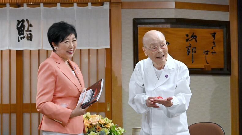 In this photo released by Bureau of Social Welfare, Tokyo Metropolitan Government, sushi legend Jiro Ono, right, shows a gift from Tokyo Gov. Yuriko Koike to celebrate his 100th birthday in front of his restaurant, Sukiyabashi Jiro in Tokyo on Sept. 18, 2025. (Bureau of Social Welfare, Tokyo Metropolitan Government via AP)