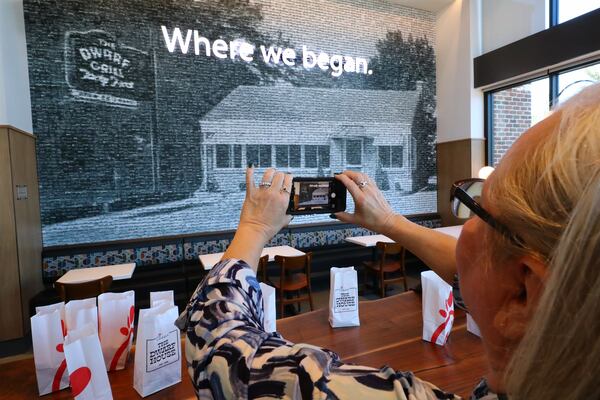 Teena Hammonds snaps a photo of an image of the original building, made up of photographs of 2,568 Chick-fil-A locations, on a wall inside Hapeville's Dwarf House, the first of Truett Cathy’s restaurants. (Curtis Compton/AJC 2022)