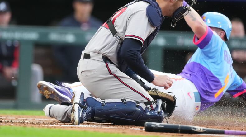 Atlanta Braves catcher Jonah Heim, front, tries to field the throw as Colorado Rockies' TJ Rumfield scores on a ground out by Willi Castro in the first inning of a baseball game Friday, May 1, 2026, in Denver. (AP Photo/David Zalubowski)