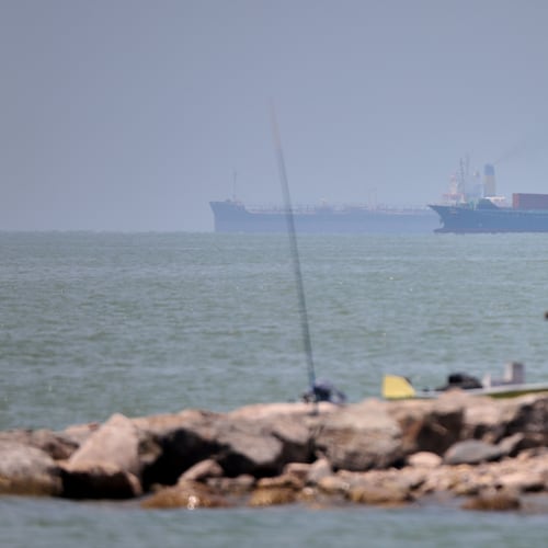 A man stands beside a fishing pole along the shore as cargo ships and commercial vessels are seen in the Strait of Hormuz off Bandar Abbas, Iran, Wednesday, June 17, 2026. (Amirhosein Khorgooi/ISNA via AP)