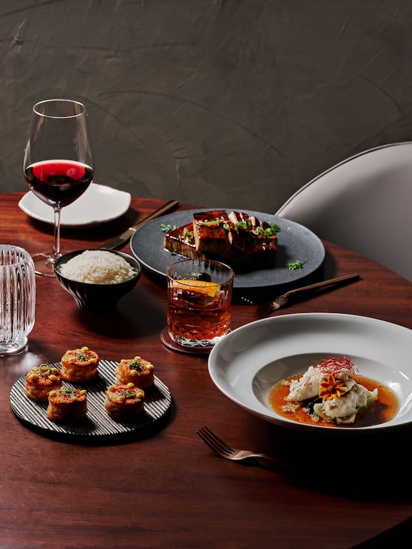 A selection of Asian dishes on a table with a glass of wine a whiskey cocktail