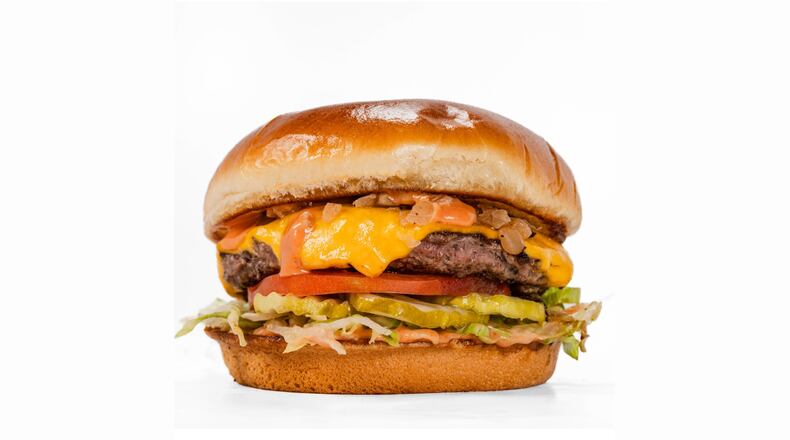 A classic-looking cheeseburger on a smooth, shiny bun, garnished with pickles, tomato slices, lettuce and a sauce.