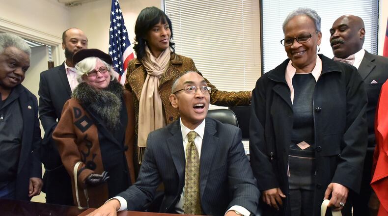 DeKalb County CEO Burrell Ellis, surrounded by his wife Philippa and supporters, takes a seat at his desk on the sixth floor of the county government building in Decatur on Wednesday after he was reinstated to office. HYOSUB SHIN / HSHIN@AJC.COM