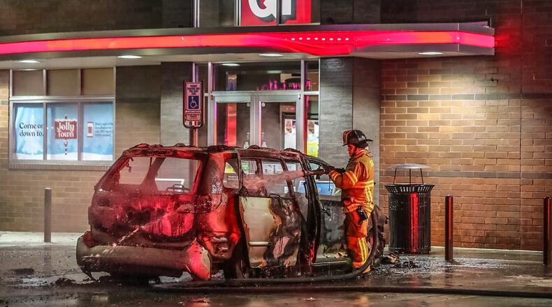 A DeKalb County firefighter douses hot spots after a minivan burst into flames Tuesday morning outside a Brookhaven QuikTrip.