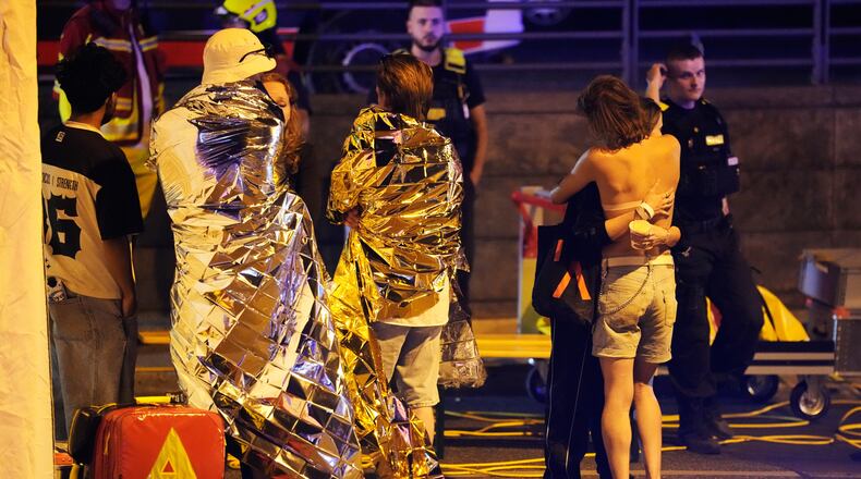 Two people embrace near others wearing thermal blankets as they stand near emergency personnel in Berlin, early Sunday, July 26, 2026, following the cancellation of Christopher Street Day festivities. (AP Photo/Markus Schreiber)