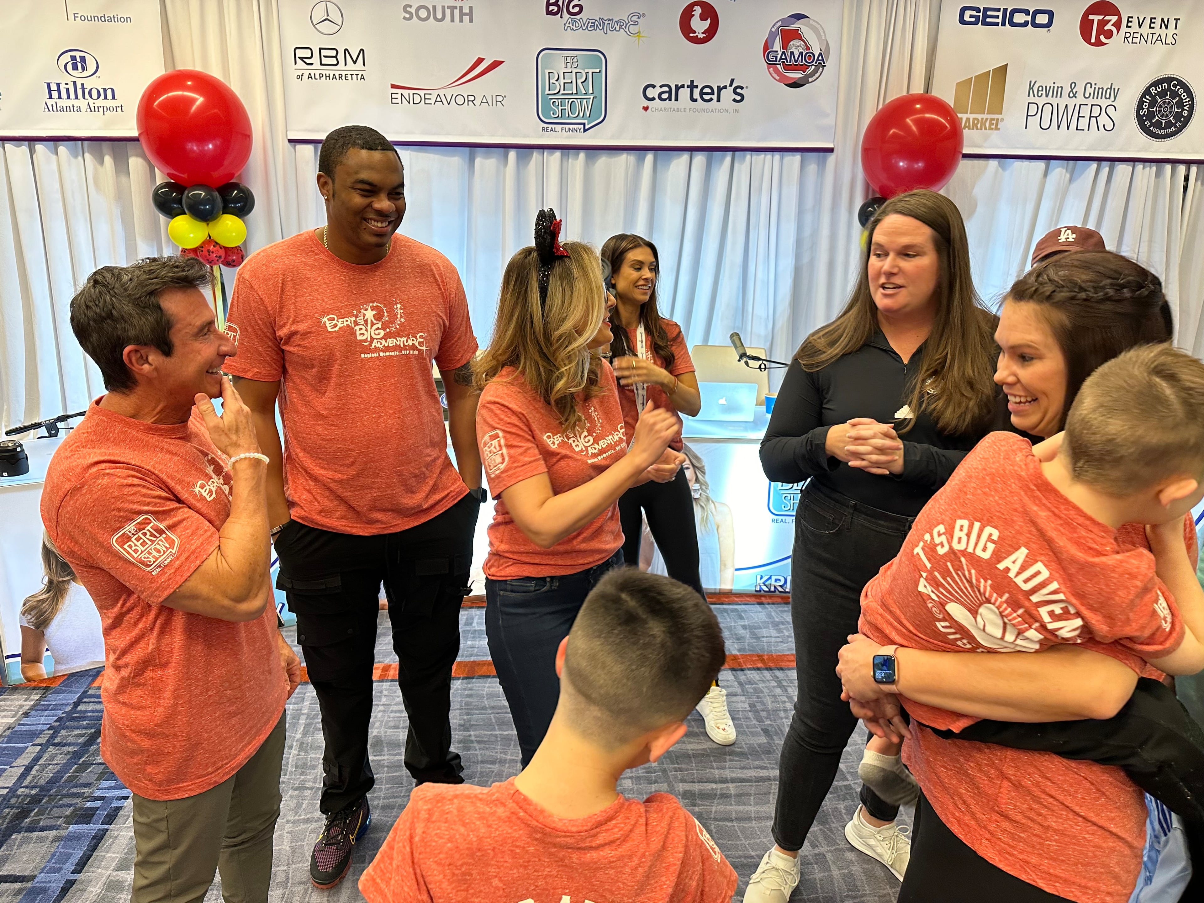Moe Mitchell (second from left) is shown with other "Bert Show" cast members, including Bert Weiss (left) and Kristin Klingshirn (center) during the annual Bert's Big Adventure kickoff party at a Hilton near the Atlanta aiport. The nonprofit takes kids with terminal or chronic illnesses to Disney World in Orlando every February. (Rodney Ho/AJC 2024)