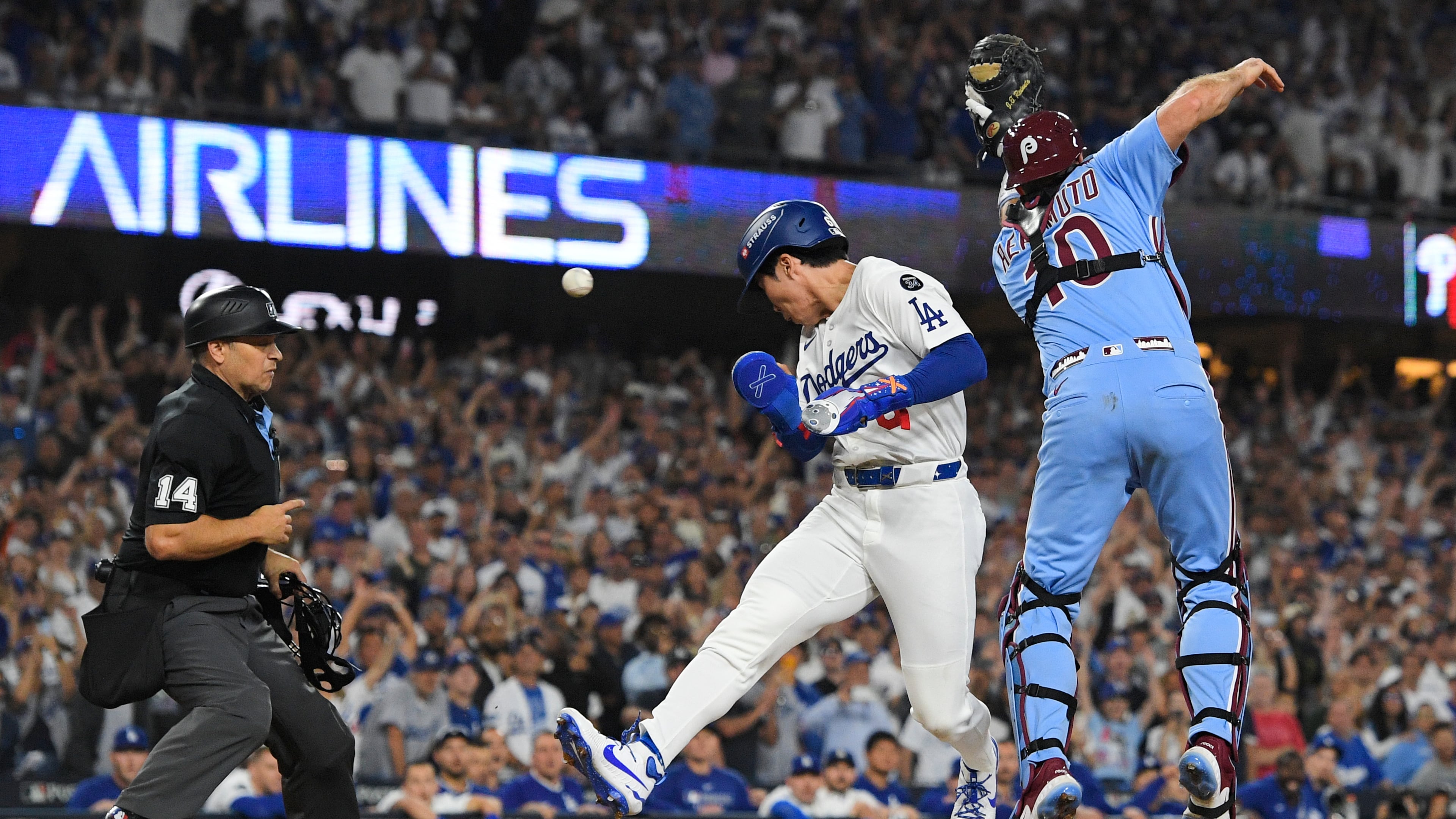 Los Angeles Dodgers' Hyeseong Kim, center, scores the game-winning run past Philadelphia Phillies catcher J.T. Realmuto (10) on a ground ball by Andy Pages and a throwing error by Phillies pitcher Orion Kerkering during the eleventh inning in Game 4 of baseball's National League Division Series Thursday, Oct. 9, 2025, in Los Angeles. (AP Photo/Mark J. Terrill)