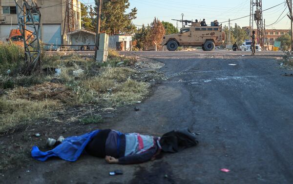 A dead fighter from the Druze militias lies on the ground, as Syrian government forces, background, deploy at Mazraa village on the outskirts of the city of Sweida, where clashes erupted between Sunni Bedouin clans and Druze militias, southern Syria, Monday, July 14, 2025. (AP Photo/Ghaith Alsayed)