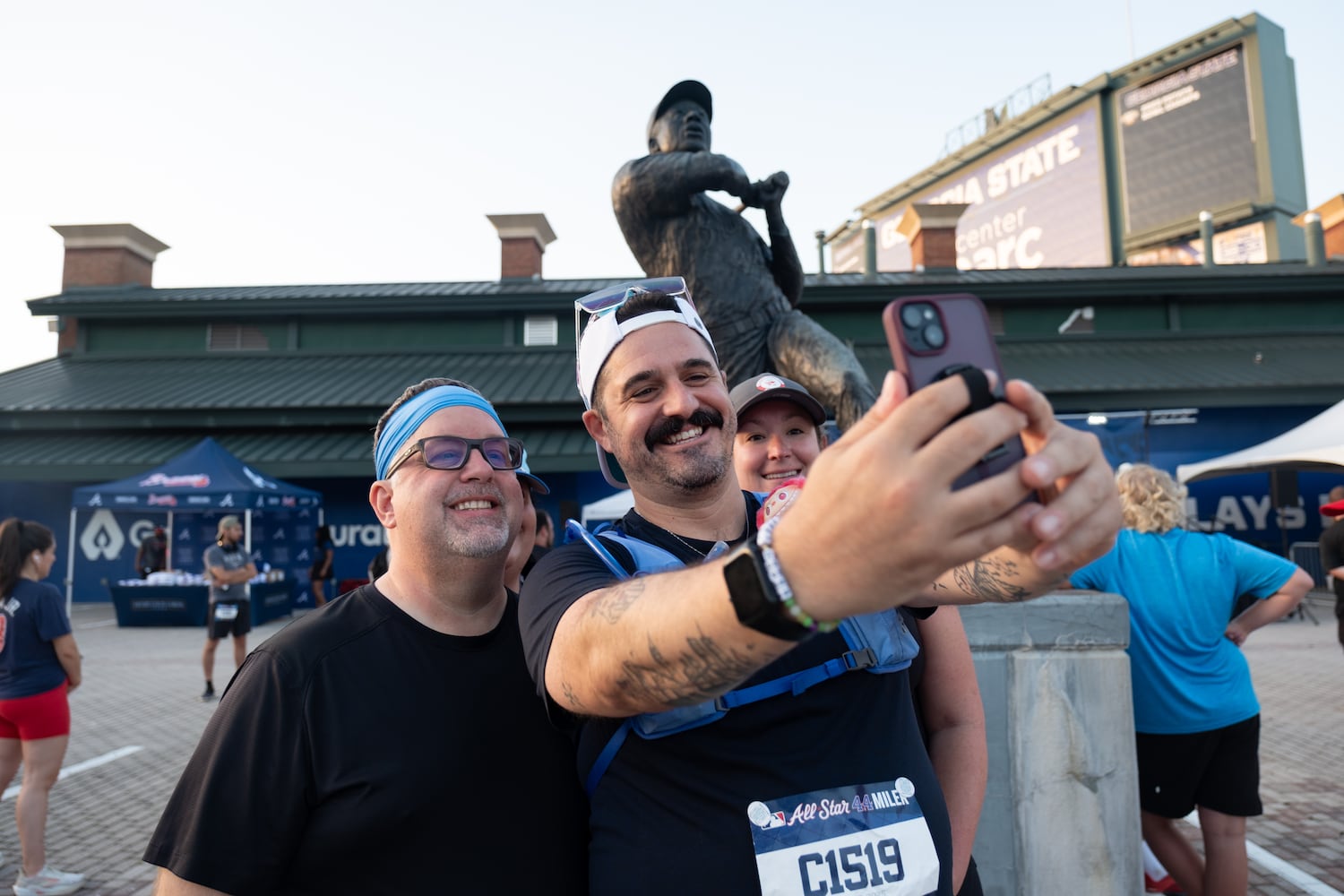 Duane Brooks, from left, Ryan Makely and Sarah Ratigan pose for a photo in front of the statue of Hank Aaron before running the MLB All-Star 4.4 Miler in Atlanta on Sunday, July 13, 2025.   Ben Gray for the Atlanta Journal-Constitution
