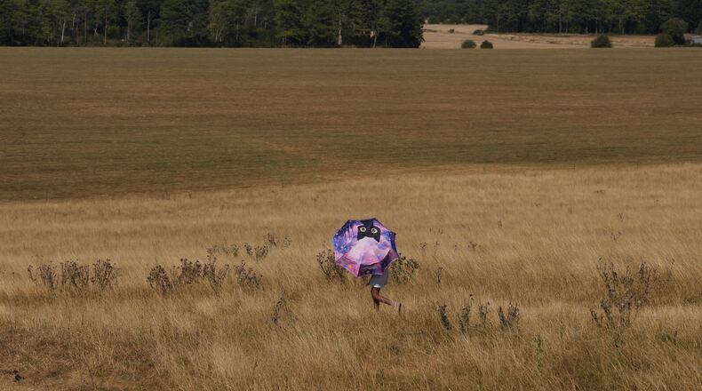 A person holds an umbrella and walks through dry grass at Stonehenge in Wiltshire, England, Thursday, Aug. 13, 2026. (AP Photo/Kin Cheung)