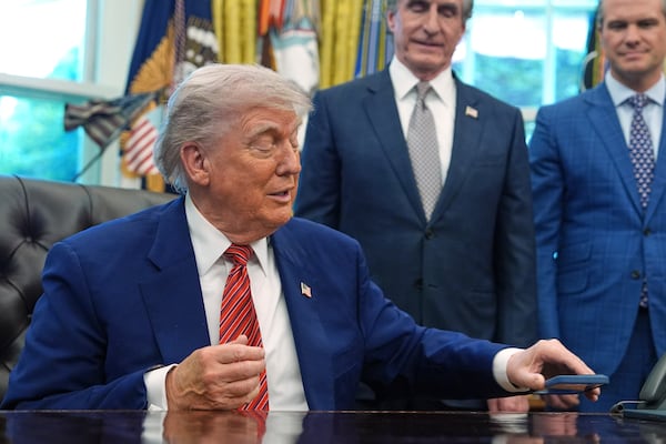 President Donald Trump silences his mobile phone which rang two times as he was speaking to reporters after signing executive orders regarding nuclear energy in the Oval Office of the White House, Friday, May 23, 2025, in Washington. (AP Photo/Evan Vucci)