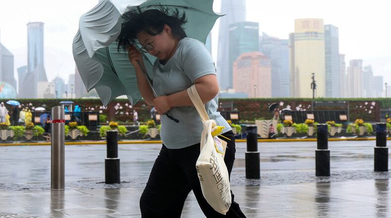 In this photo released by Xinhua News Agency, a woman struggles with her umbrella in strong wind and rain ahead of Typhoon Dolphin at Huangpu District of Shanghai on Sunday, Aug. 9, 2026.(Wang Xiang/Xinhua via AP)