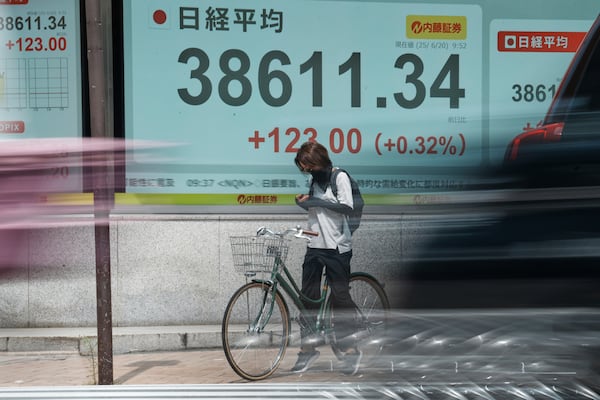 A person waits a traffic signal in front of an electronic stock board showing Japan's Nikkei index at a securities firm Friday, June 20, 2025, in Tokyo. (AP Photo/Eugene Hoshiko)