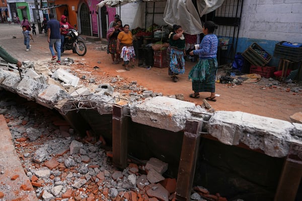 Residents walk past debris from damaged houses in Santa Maria de Jesus, Guatemala, Wednesday, July 9, 2025, following dozens of earthquakes and aftershocks that were recorded in a matter of hours. (AP Photo/Moises Castillo)
