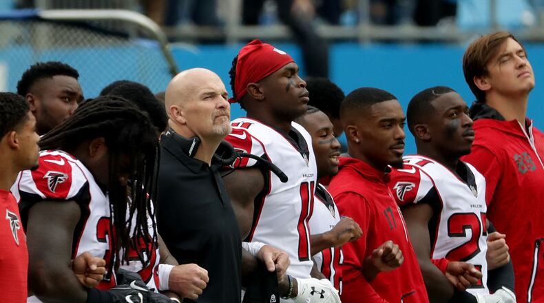 Falcons head coach Dan Quinn links arms with his team during the national anthem against the Panthers at Bank of America Stadium on Sunday in Charlotte, North Carolina.