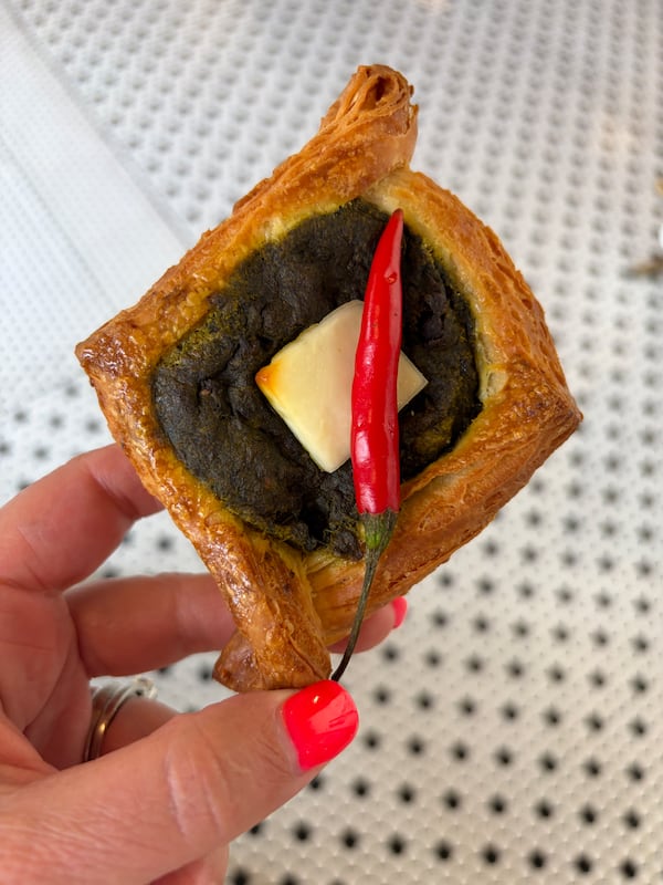 A danish pastry filled with savory saag paneer, the piece of paneer placed directly in the center so its surrounded by the green spinach gravy, and topped with a red pepper.