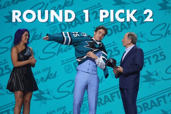 Michael Misa, middle, puts on a jersey between WWE wrestler Bayley, left, and NHL commissioner Gary Bettman after being drafted by the San Jose Sharks during the NHL hockey draft Friday, June 27, 2025, in Los Angeles. (AP Photo/Damian Dovarganes)