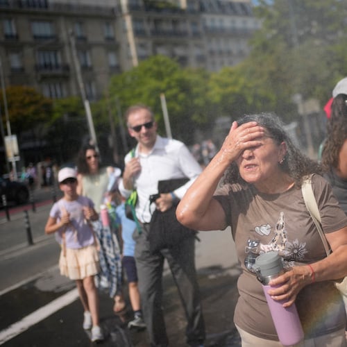Tourists enjoy cooling off at a public water fountain In Paris, Friday, June 26, 2026. (AP Photo/Christophe Ena )