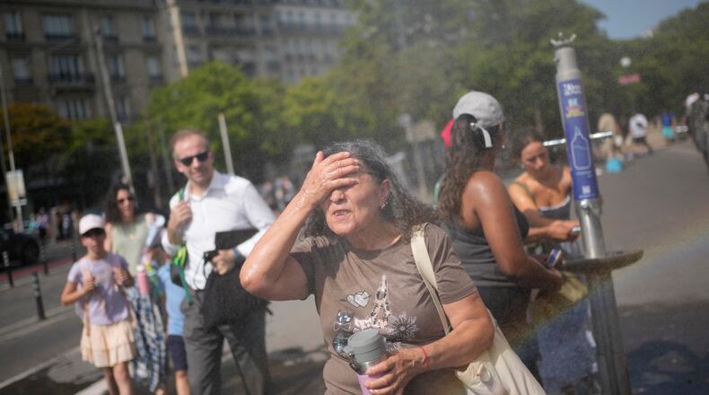 Tourists enjoy cooling off at a public water fountain In Paris, Friday, June 26, 2026. (AP Photo/Christophe Ena )