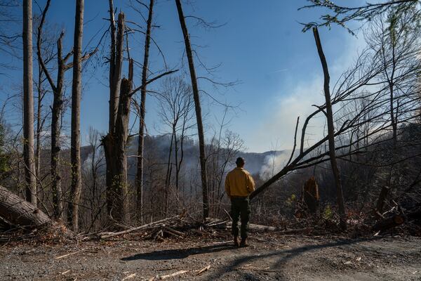 Hector Medrano, a firefighter from California, stands in the midst of debris from Hurricane Helene as coordinates a helicopter water drop for the wildfires Wednesday, March 26, 2025, in Saluda, N.C.. (AP Photo/Allison Joyce)