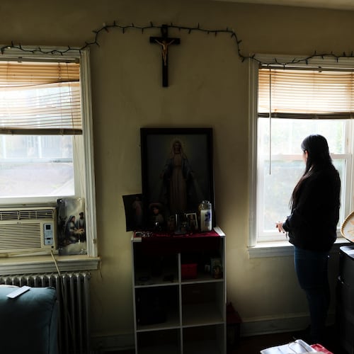 A parishioner of the Shrine of the Sacred Heart, whose husband was detained by immigration agents, looks out her home's window as she poses for a portrait in Washington, Friday, Oct. 10, 2025. (AP Photo/Luis Andres Henao)