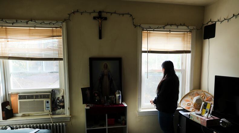 A parishioner of the Shrine of the Sacred Heart, whose husband was detained by immigration agents, looks out her home's window as she poses for a portrait in Washington, Friday, Oct. 10, 2025. (AP Photo/Luis Andres Henao)