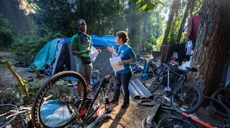 Intown Cares homeless services team leader Tracy Woodard talks with Ladell Hassell about an upcoming free medical care opportunity at an encampment used by individuals experiencing homelessness along the banks of the North Fork of Peachtree Creek near Buford Highway on Tuesday, August 22, 2023. The 24-year-old struggled to replace a bike tire so he could hit the streets in search of water as temperatures climbed.  (Steve Schaefer/steve.schaefer@ajc.com)