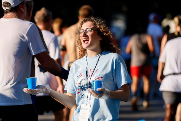 A volunteer hands out water at the Peachtree Road Race. "One common mistake is waiting for thirst, an emergency response to low blood volume, to drink," Dan Benardot, a professor at Emory University's Center for the Study of Human Health, tells the AJC. (Abbey Cutrer/AJC 2025)