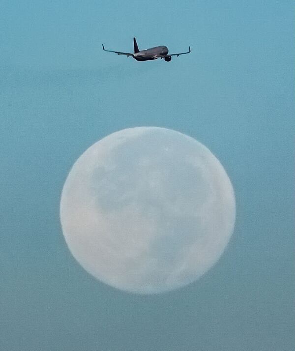 A plane seemingly hovers over the blue moon, which is one of four supermoons in 2024, as it takes off from the Atlanta airport.