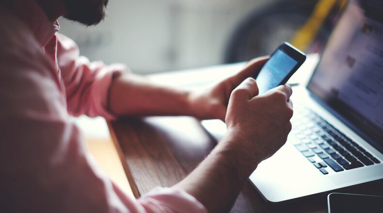 A man using a cell phone at an office desk by a wooden table. (Dreamstime/TNS)