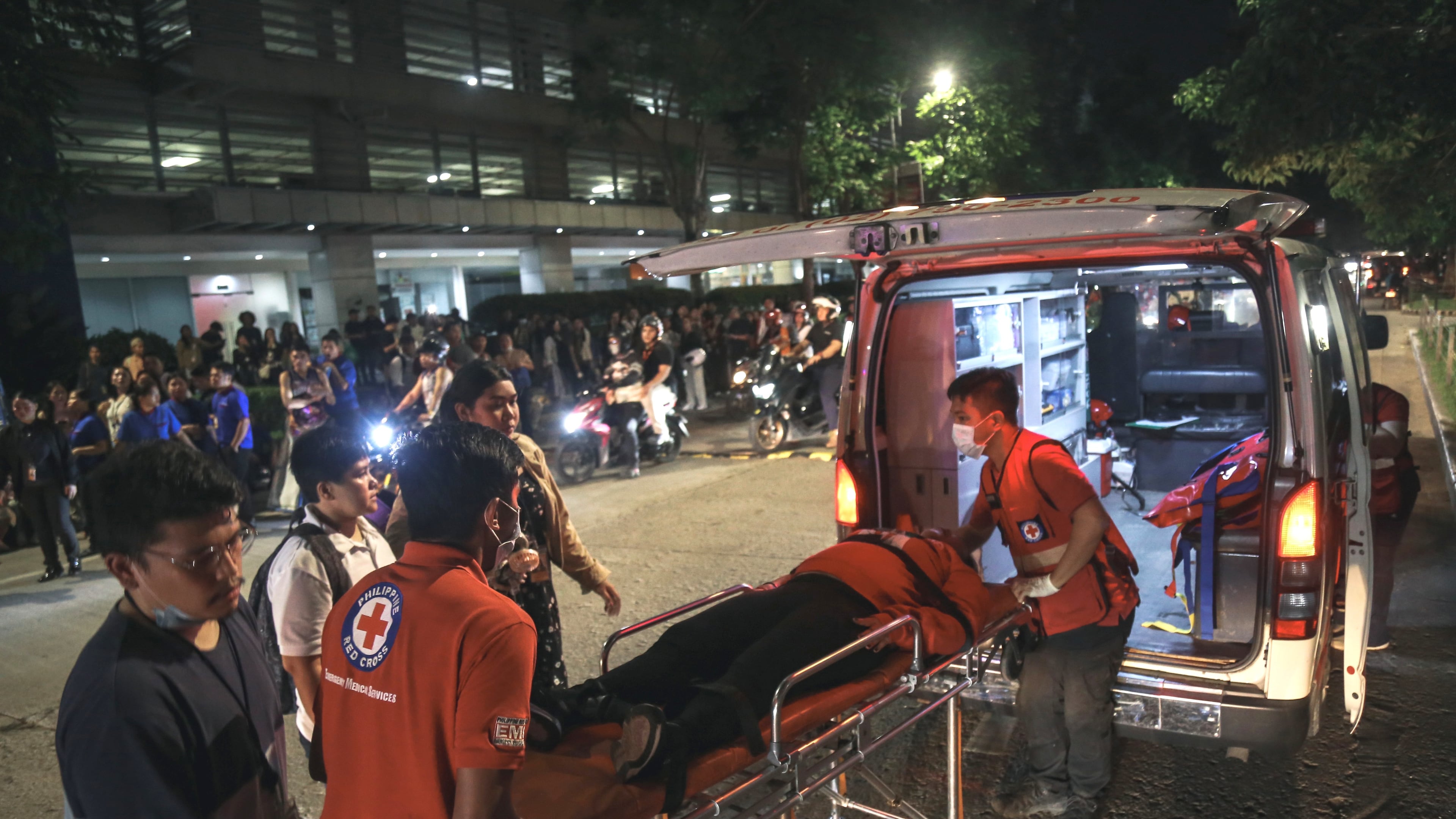 Medical workers load a resident into an ambulance as others stay outside buildings after a strong earthquake struck Cebu city, central Philippines, on Tuesday, Sept. 30, 2025. (AP Photo/Jacqueline Hernandez)