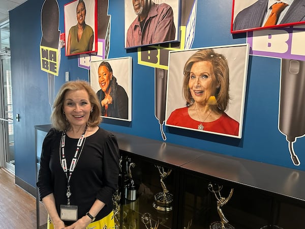 Lois Reitzes stands by her impish official  photo in the waiting room at WABE headquarters on May 9, 2025. (Rodney Ho/AJC)