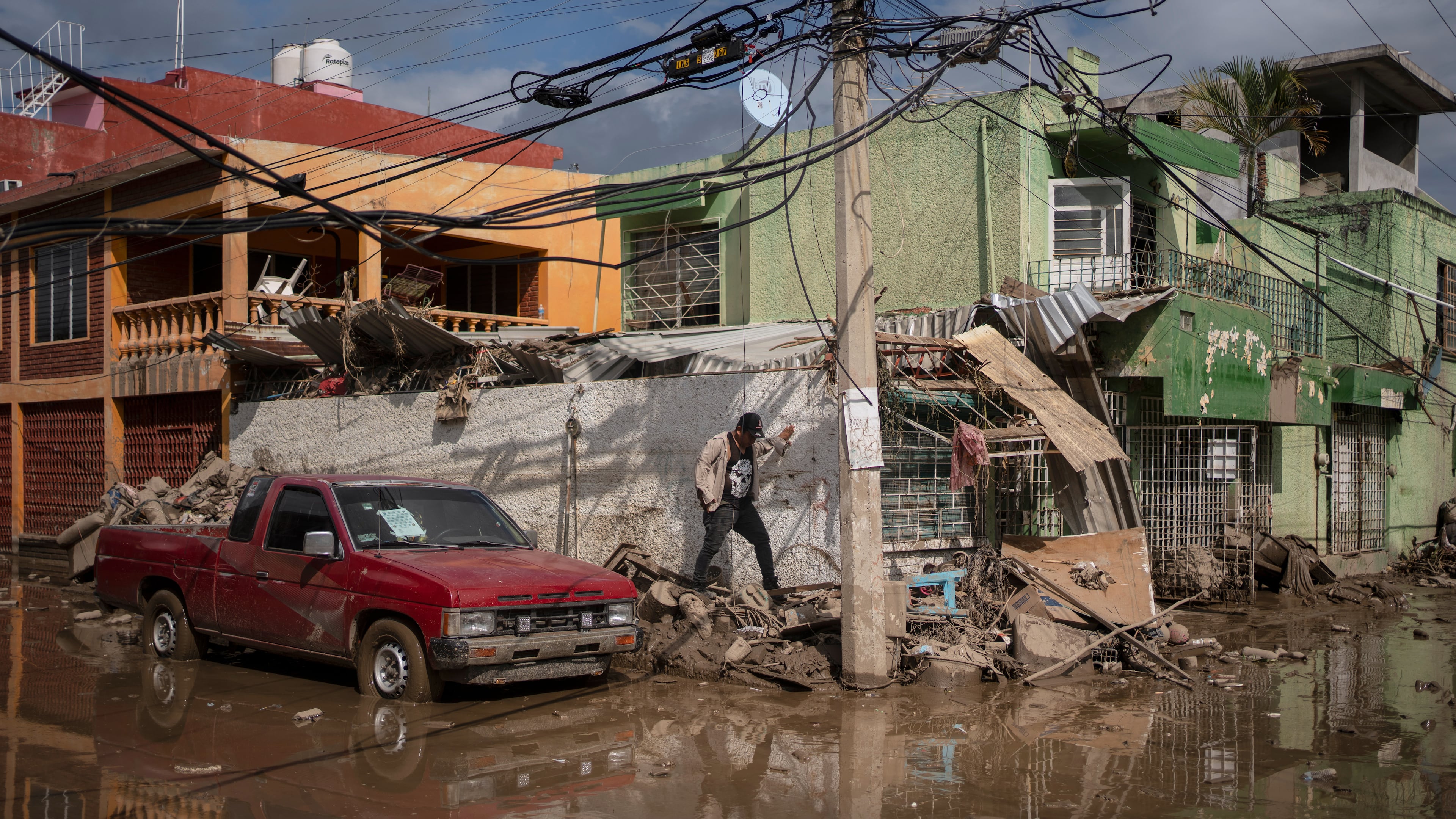 A local walks along a mud-covered street in Poza Rica, Veracruz state, Mexico, on Tuesday, Oct. 14, 2025, after landslides and torrential rain. (AP Photo/Felix Marquez)