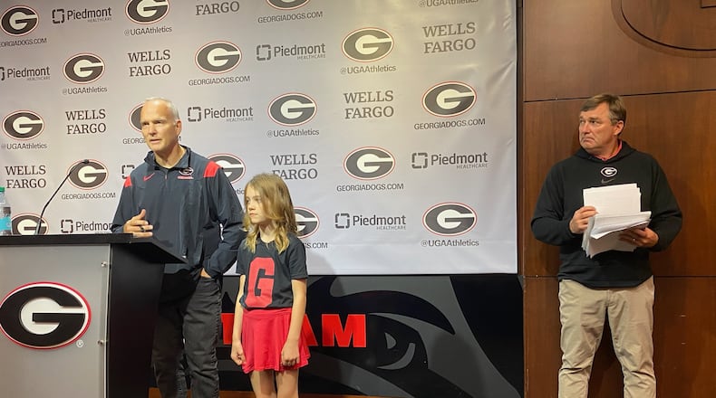 Former Georgia football coach Mark Richt speaks to media in Butts-Mehre Heritage Hall Oct. 14, 2024, accompanied by granddaughter Jadyn Richt, while Bulldogs coach Kirby Smart looks on. (AJC photo by Ken Sugiura)