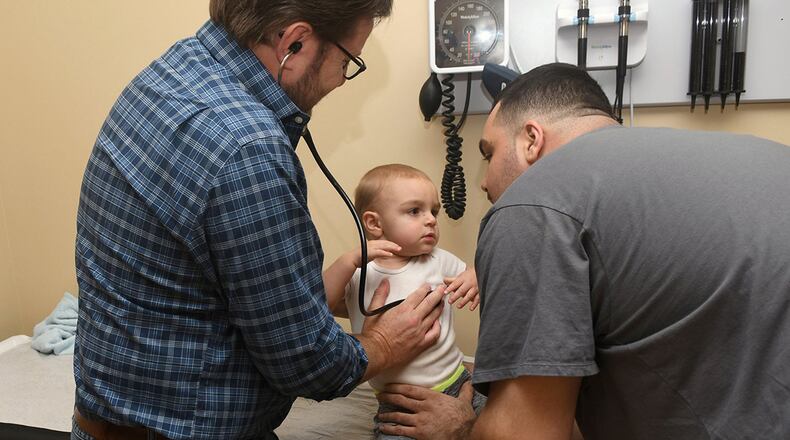 Dr. Greg McHan examines Lenny Falletta III, 18 months, of Blairsville with a little help from Lenny’s dad last month at the Georgia Mountains Health clinic in Blue Ridge. The clinic network needs to hire another pediatrician but has put the brakes on that process because it doesn’t know whether Congress will renew its funding. Nationwide, one-quarter of all such clinics have already taken a hit to their personnel because of this uncertainty. (Photo special to the AJC by Rebecca Breyer)