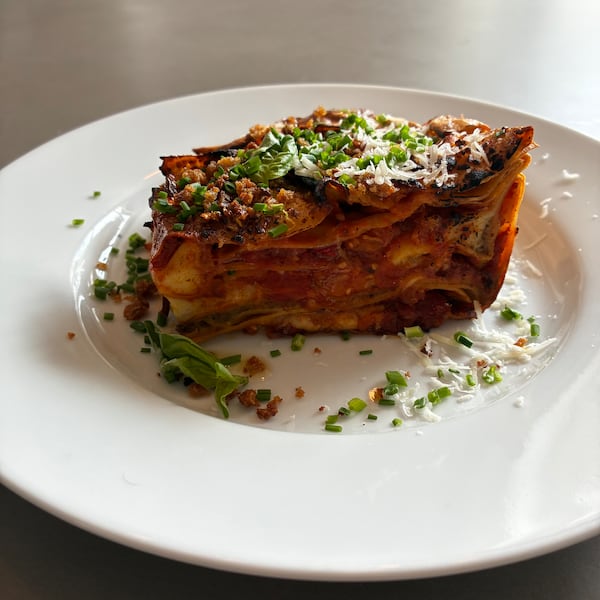 A wedge of lasagna with about 5 layers of noodles, sauce and vegetables. The top is sprinkled with fresh herbs and parmesan cheese.