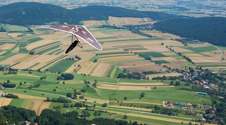 A hang glider soars above the countryside enjoying a beautiful vista of the earth below.