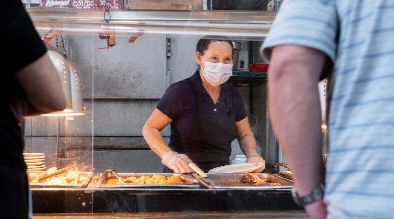Marie Rodriguez helps a customer from behind acrylic panels during the lunch rush at Matthews Cafeteria on Main Street in Tucker on July 17, 2020. The dining institution, established in 1955, ask customers to wear masks, added the acrylic dividers, made separate entrance and exit doors and have drive-up service.