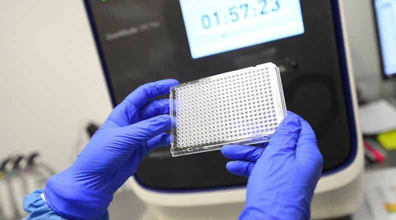 A lab worker holds a plate that will hold samples of possible COVID-19 and be put in the machine behind it to be analyzed at Ipsum Diagnostics labratory on Monday, March 23, 2020. JOHN AMIS / FOR THE AJC