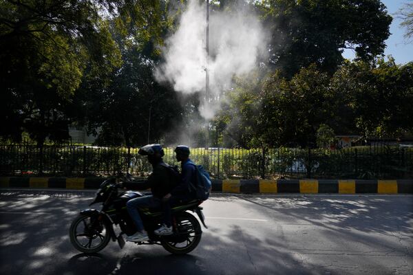 FILE - A motorcyclist drives past sprinklers that spray water in hopes of settling dust and calming air pollution in New Delhi, Feb. 12, 2025. (AP Photo/Manish Swarup, File)