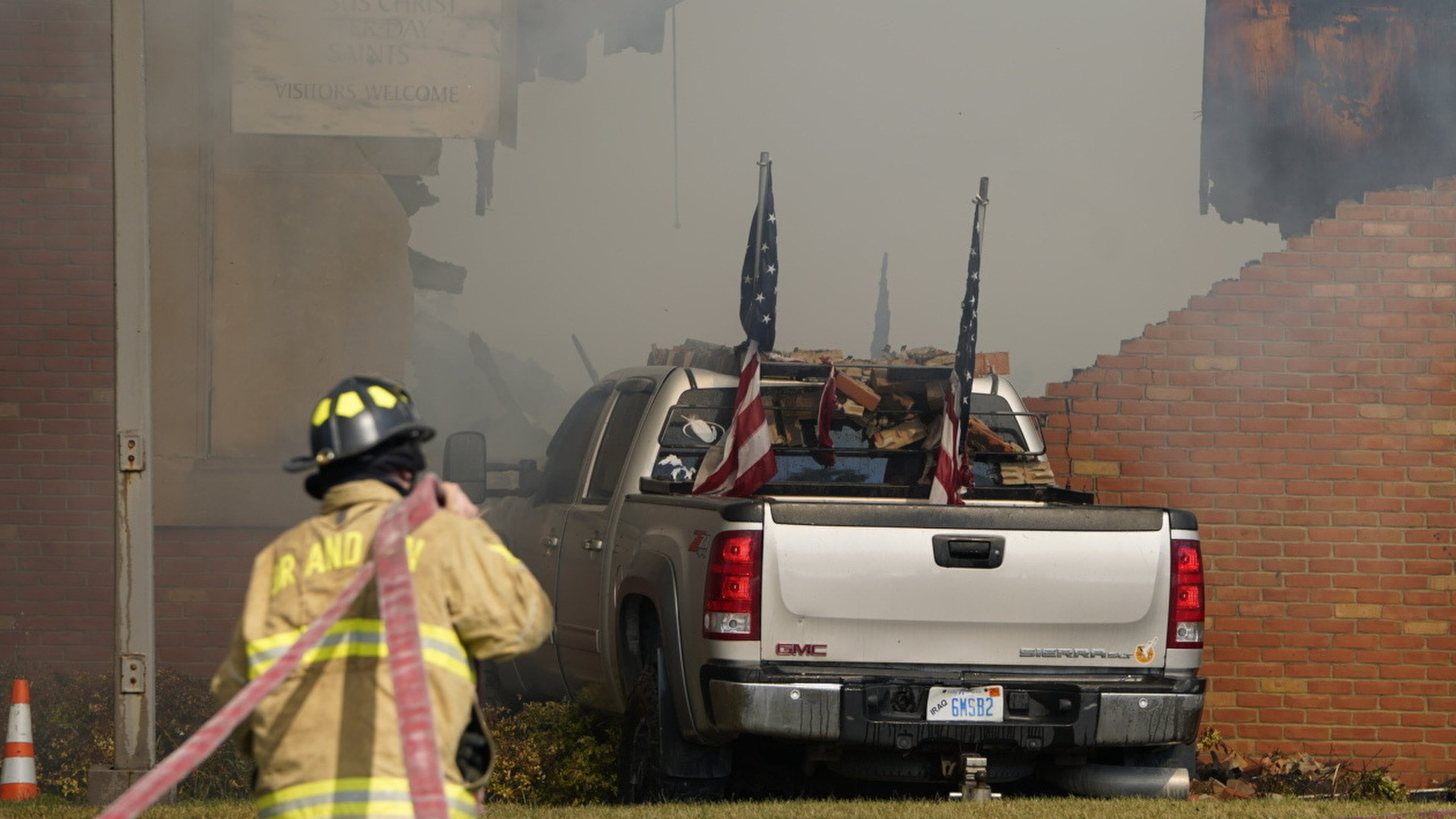 A vehicle that was rammed into the building is surrounded by smoke as a firefighter works on the scene at the Church of Jesus Christ of Latter-day Saints in Grand Blanc, Mich., Sunday, Sept. 28, 2025. (Lukas Katilius/The Flint Journal via AP)